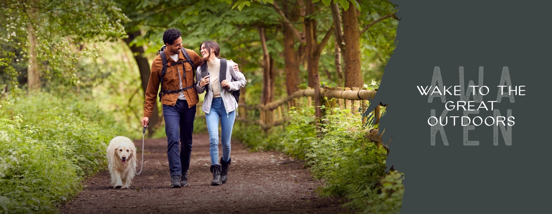 a man and woman walking a dog on a trail in the woods